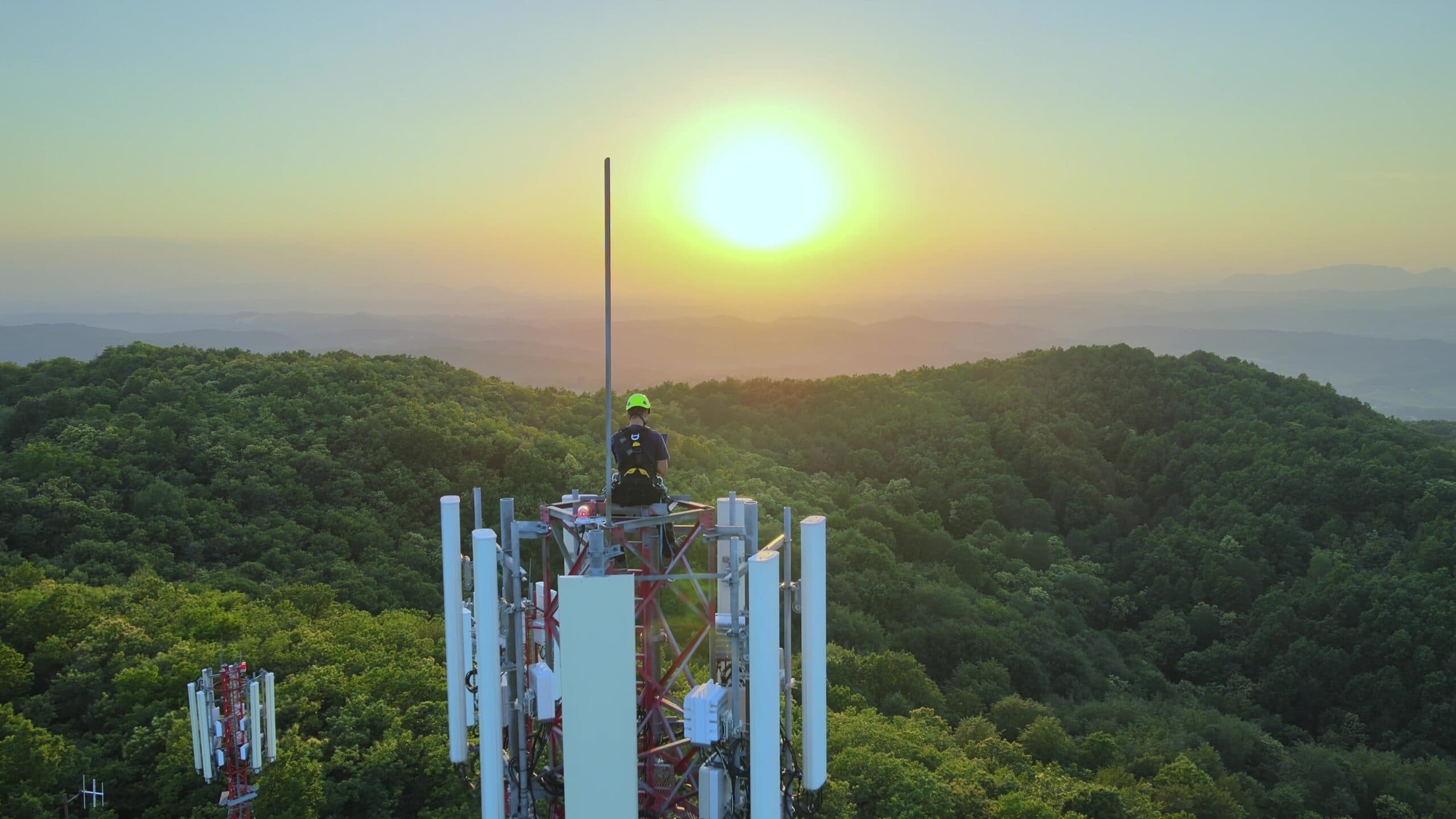 Técnico en lo alto de una antena de telecomunicaciones al atardecer